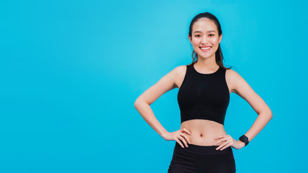 Portrait of confident beautiful asian fitness woman standing after exercise isolated on blue colour background with copy space.Concept of slim and healthy happy girl workout.