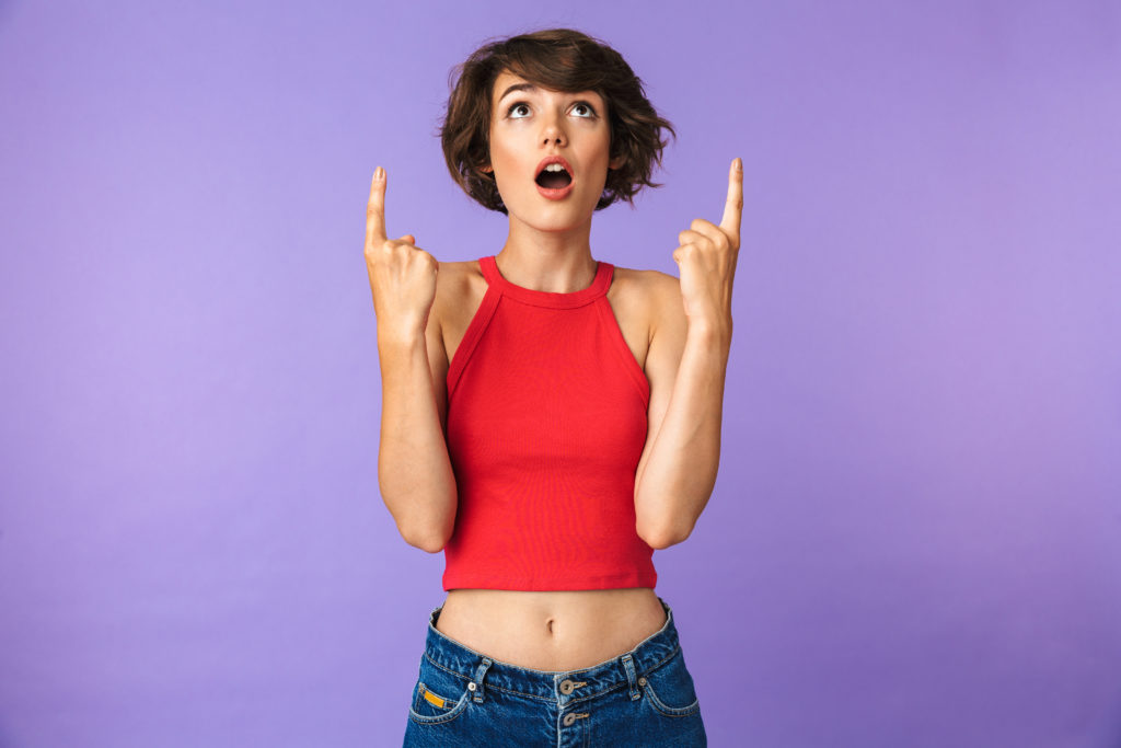 Image of excited woman 20s in casual wear pointing fingers upward at copyspace with open mouth isolated over violet background