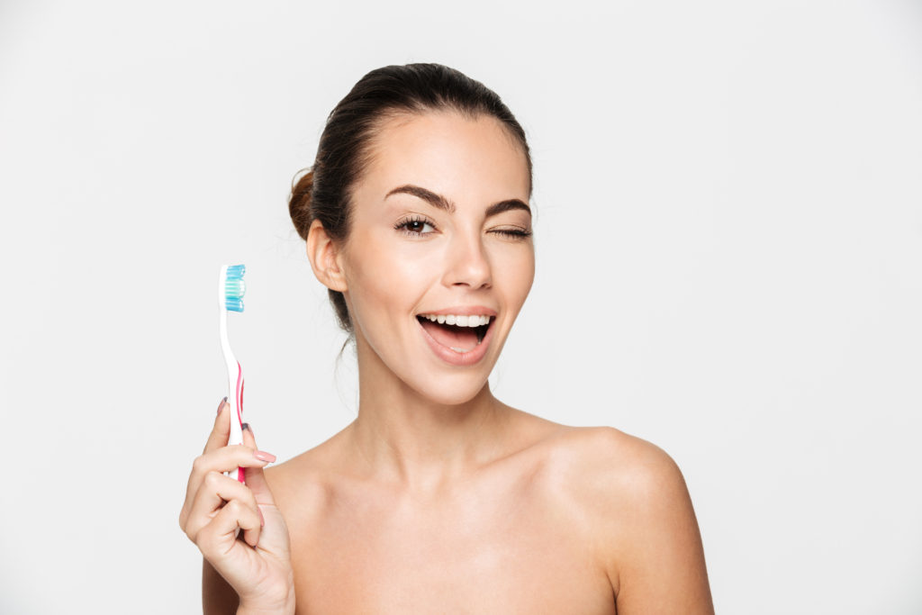 Beauty portrait of a smiling beautiful half naked woman holding toothbrush and winking isolated over white background