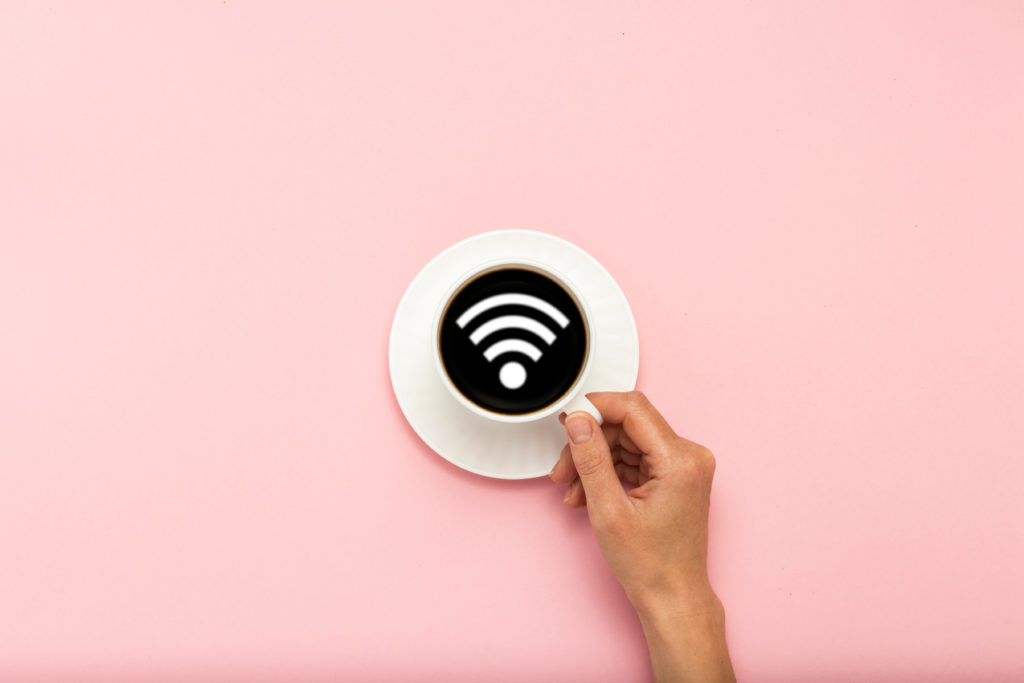 Female hand holding a white cup with black coffee on a pink background. WiFi sign. Flat lay, top view.