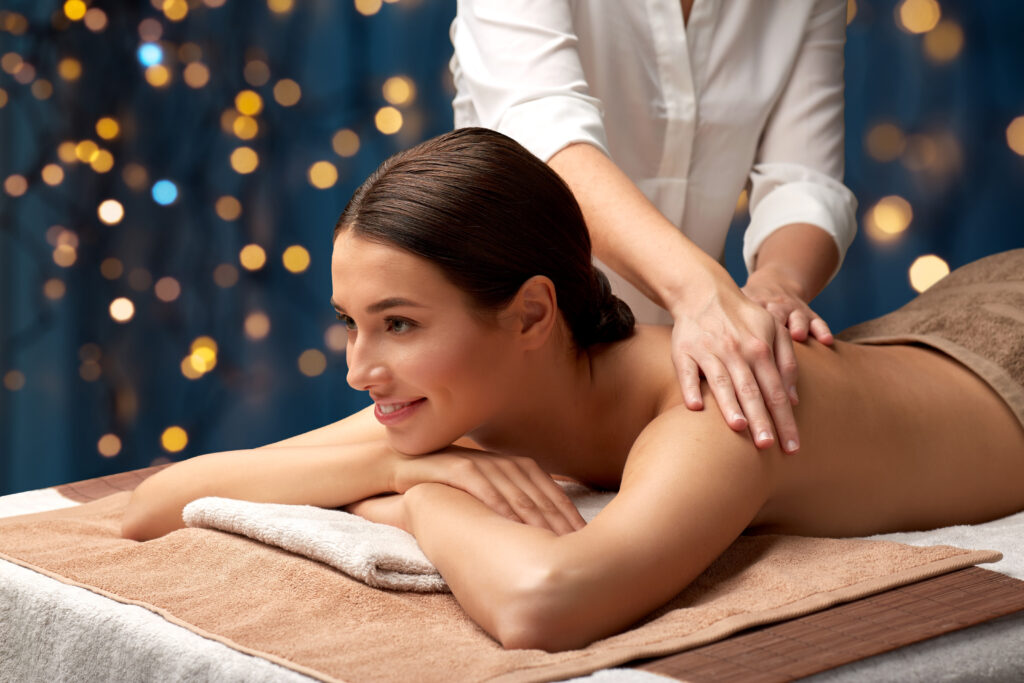 wellness, beauty and relaxation concept - beautiful young woman lying and having back massage at spa over golden lights on blue background