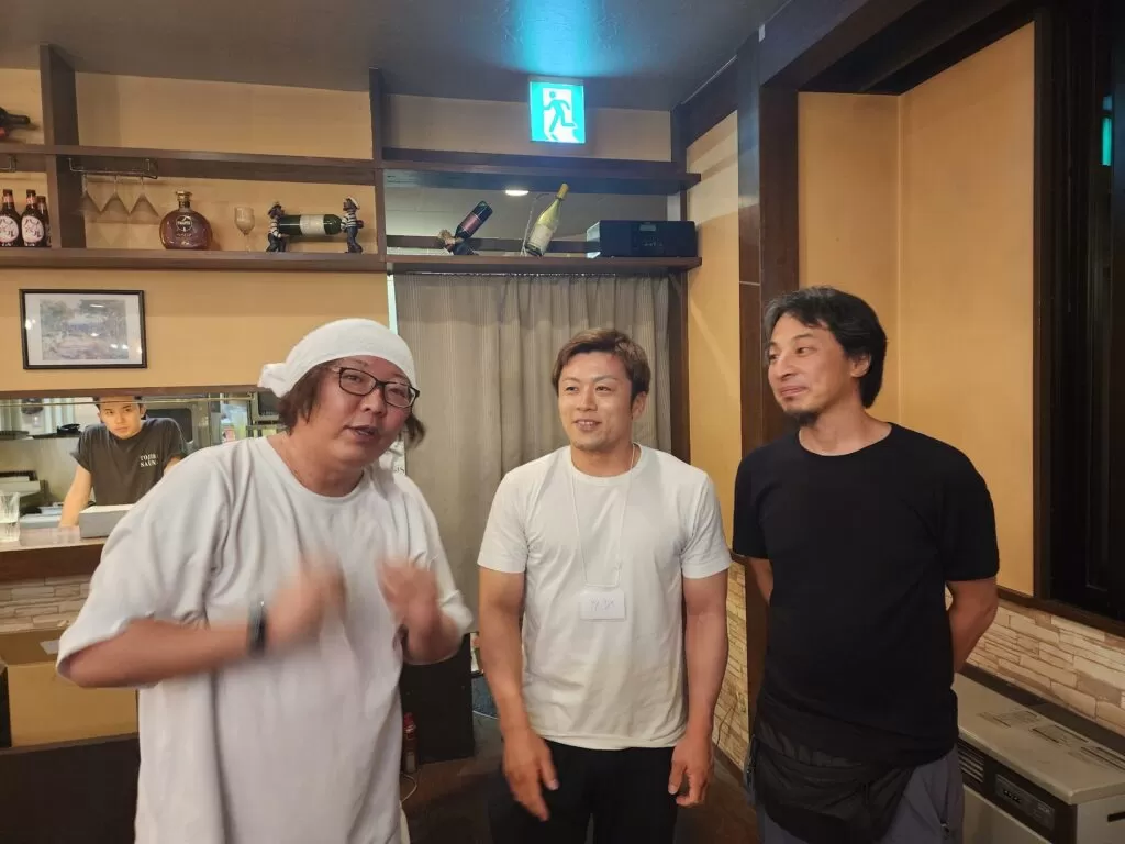 カメラを向けると手が残像になるくらいのスピードでタオルを装着するひげおやじさんとそれを見る筆者とひろゆき氏